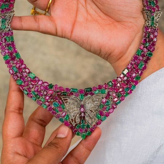 Necklace with butterfly design held by a hand against a neutral background in natural rubies and natua emerald with single cut dimonds
